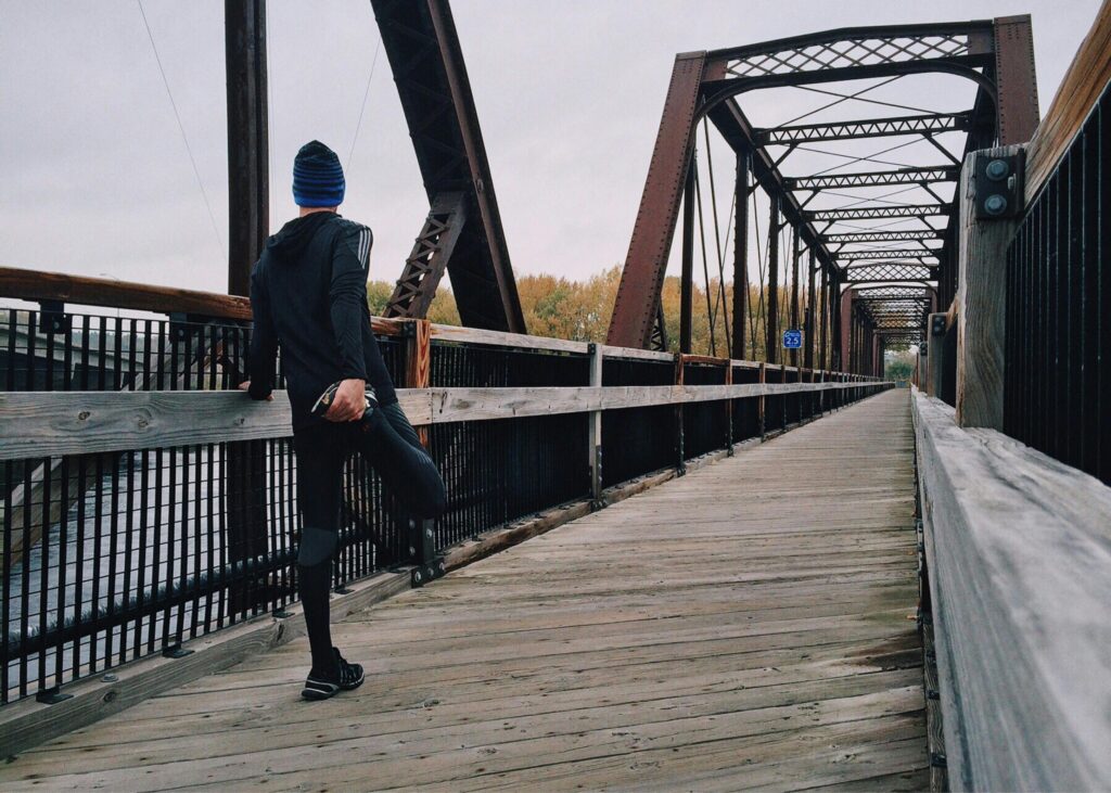 Man stretching on a wooden footbridge during a daytime run on an iron bridge, emphasizing fitness and recreation.