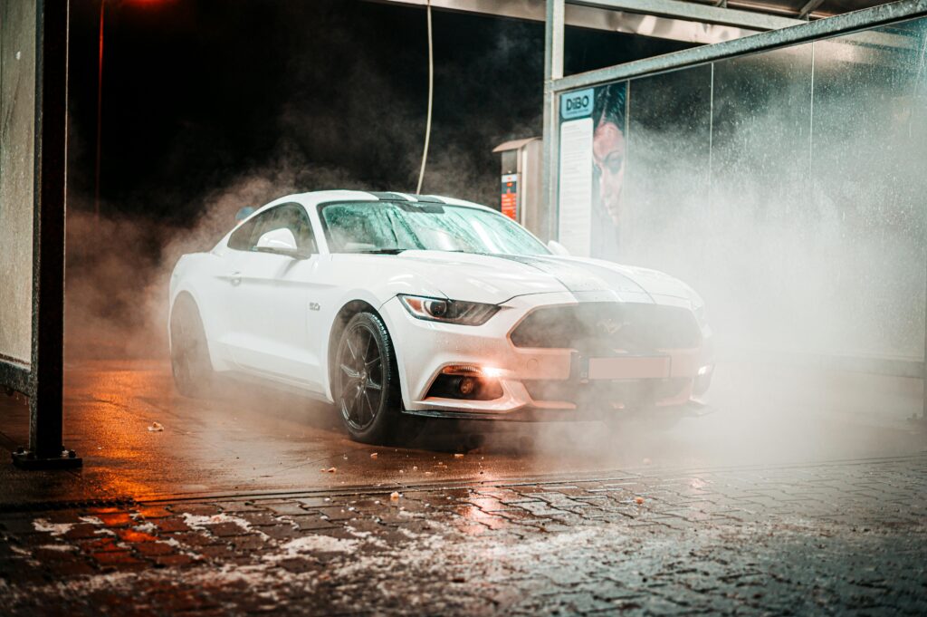 White Ford Mustang in a misty carwash setting, illuminated at night in an urban environment.