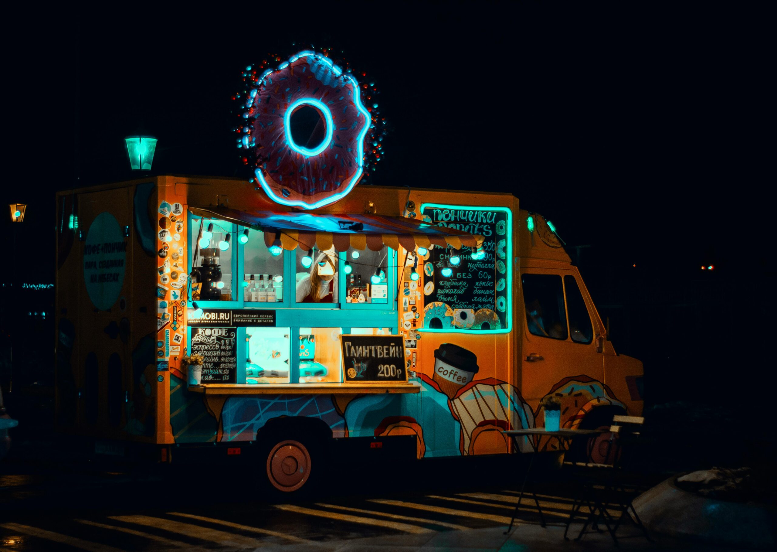 Vibrant neon food truck at night serving snacks with glowing donut sign.